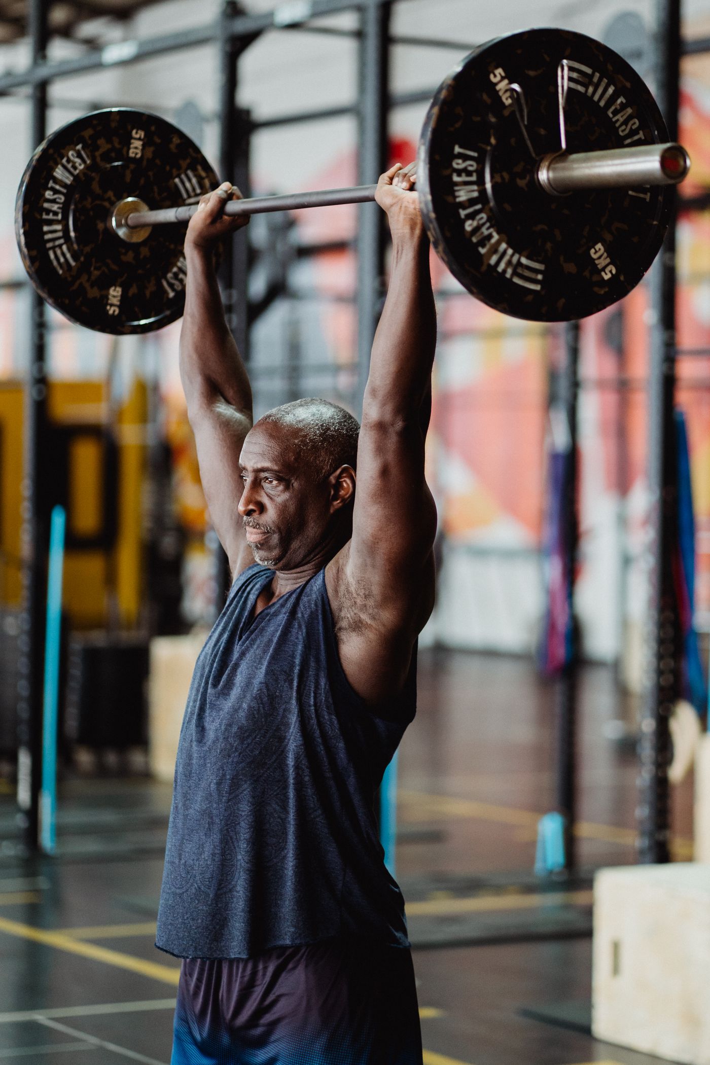 A still-training adult pressing a barbell overhead.